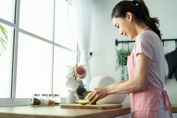 Asian attractive woman wear apron cook green salad in kitchen at home. Young beautiful girl feeling happy and enjoy eating vegetables healthy foods to diet and lose weight for health care in house. - Foto, immagini