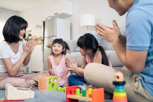 Ázsiai boldog család ül a földön, játszani gyerek játék együtt a nappaliban. Vonzó szülők anya és apa töltenek egy kis időt fiatal lányok a házban. Tevékenységi viszony az otthoni koncepcióban. - Fotó, kép
