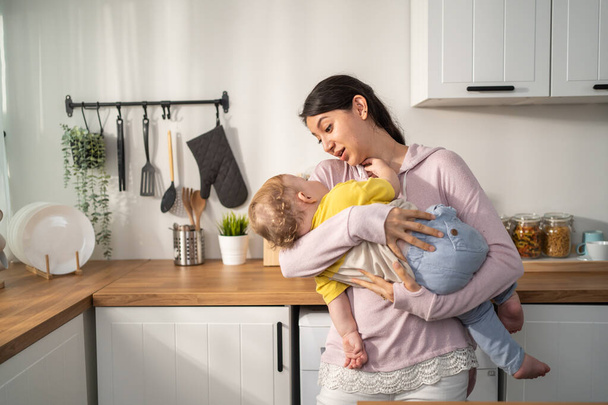 Caucasian loving mother hold baby boy toddler to lull him to sleep. Attractive mom carry little kid son with gentle and tenderness for healthy daytime nap in house. Motherhood-parenting concept. - Фото, зображення