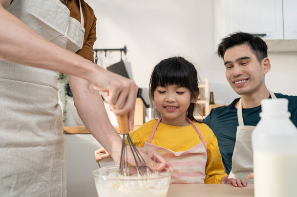 Asian attractive LGBTQ gay family teach girl kid making yeast dough. Handsome male couple take care and spend time with little adorable child bake bakery in kitchen, enjoy parenting activity at home. - Photo, Image