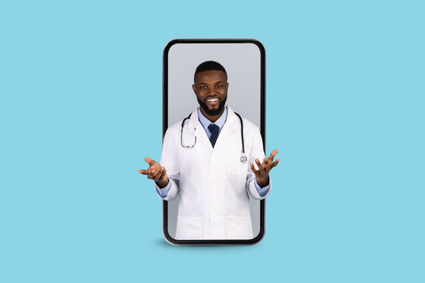 Online Medicine. Smiling Black Doctor Peeking Out Of Big Smartphone Screen - Photo, image