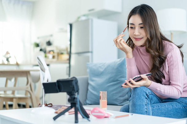 Asian professional woman artist stay home, enjoying makeup herself. Young attractive beautiful girl sit on sofa, feel happy look to mirror and coloring eyebrows on face enjoy beauty cosmetic in house. - Φωτογραφία, εικόνα