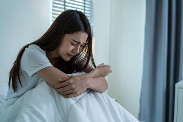 Asian beautiful depression girl crying in tears sit on bed in bedroom. Attractive unhappy young woman feeling sad lonely and upset with life problem and hold tissue on hands in dark night room at home - Zdjęcie, obraz