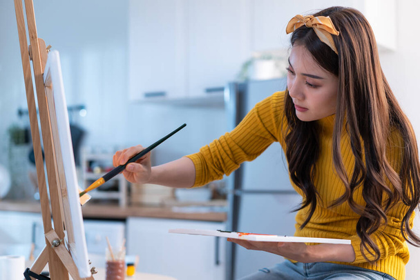 Asian young talented woman artist coloring on painting board in house. Attractive beautiful female draw art picture, creating artwork with watercolor paint and brush enjoy creativity activity at home. - Photo, Image