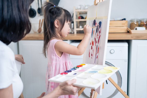 Asian young happy kid daughter coloring on painting board with mother. Happy family activity, Little girl child learn how to draw art picture with watercolor paint and brush enjoy creativity with mom. - Fotoğraf, Görsel
