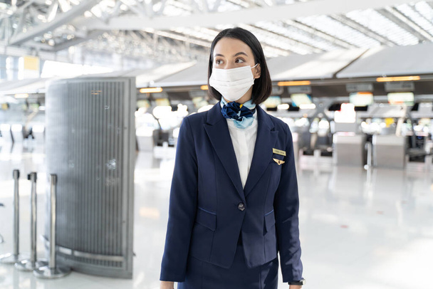 空港ターミナルに立つ白人客室乗務員の肖像。魅力的な美しい客室乗務員や顔マスクを身に着けている空気のホステスの女性は、 Covi19パンデミック危機の間に飛行機で働く準備. - 写真・画像