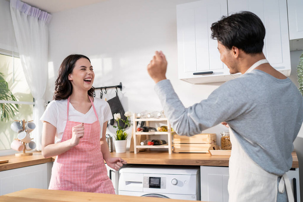 Asian attractive loving couple enjoy dance together in kitchen at home. Beautiful romantic new marriage man and woman wear aporn feeling happy and enjoy activity relationship in house listen to music. - Фото, изображение