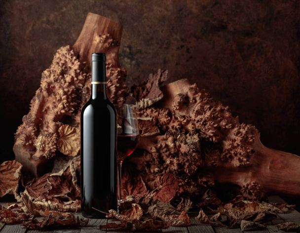 Пляшка і келих червоного вина на старому дерев'яному столі. На задньому плані старі сноби і висушені листя лози. Копіювати простір
. - Фото, зображення