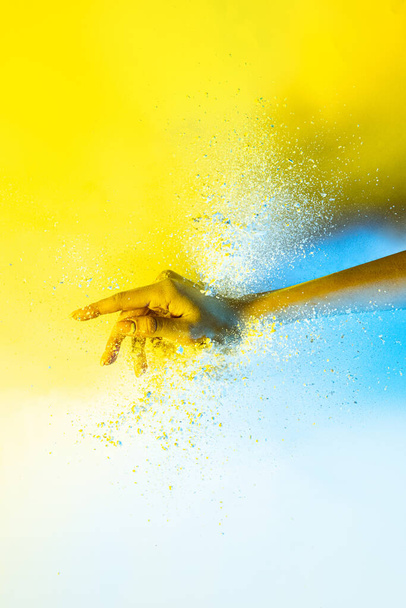 Yellow and white. Female hand and explosion of colored, neoned powder on bright studio background with copy space. Magazine cover, wallpaper design - Фото, зображення
