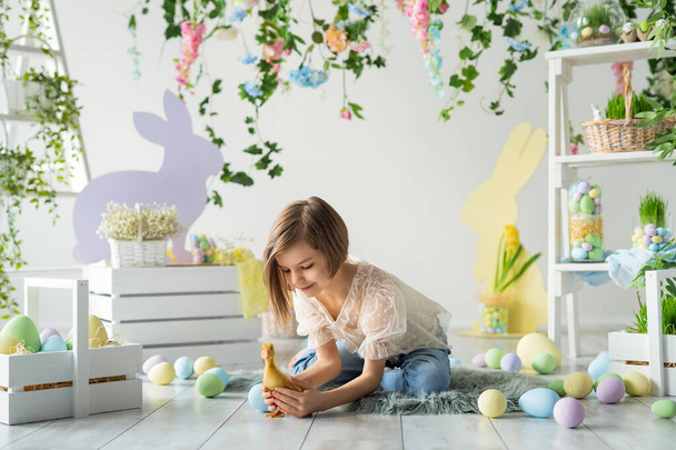 Little girl plays and communicates with duckling while sits on the floor. Easter decoration.  - Valokuva, kuva