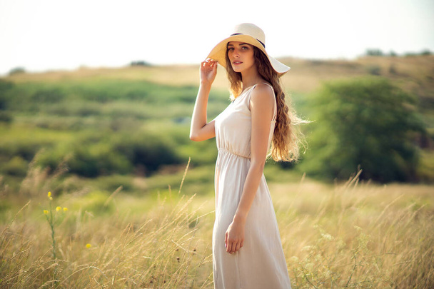 young pretty woman walks on field in summer while wearing a sunhat and midi dress. Lifestyle  - Фото, изображение