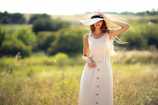 young beautiful woman stands on field in summer while wearing a sunhat and midi dress. Lifestyle  - Zdjęcie, obraz