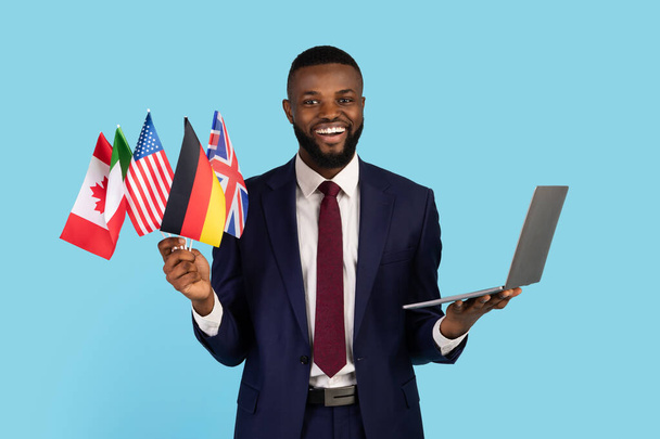 ビジネス言語コース。黒のビジネスマンが旗とノートパソコンの束を保持 - 写真・画像