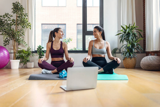 Shot of two sporty young women doing exercises following online gym classes via laptop on floor at home. - Φωτογραφία, εικόνα