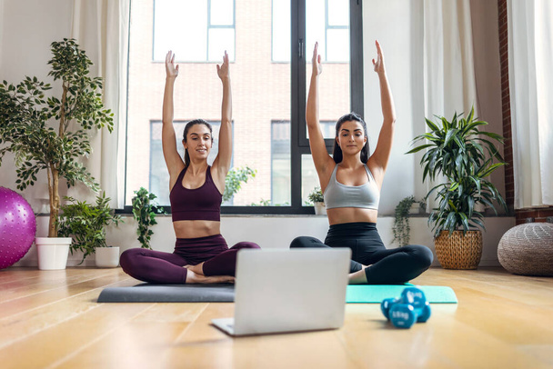 Shot of two sporty young women doing exercises following online gym classes via laptop on floor at home. - Фото, зображення