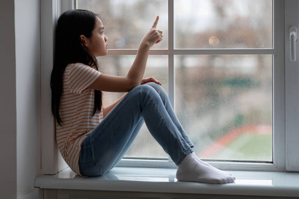 Side view of frustrated chinese girl sittng on windowsill - Foto, Imagem