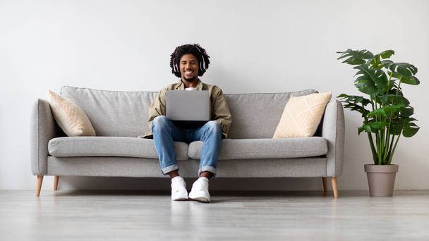 Happy African American Guy Wearing Wireless Headphones Relaxing With Laptop At Home - Фото, зображення