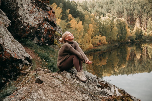 A young blonde girl walks in the autumn in the mountains with a view of the river and forest - Foto, immagini