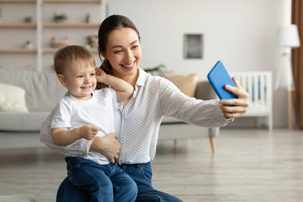 Young happy mother taking selfie with her adorable toddler son, spending time together at home - Fotografie, Obrázek