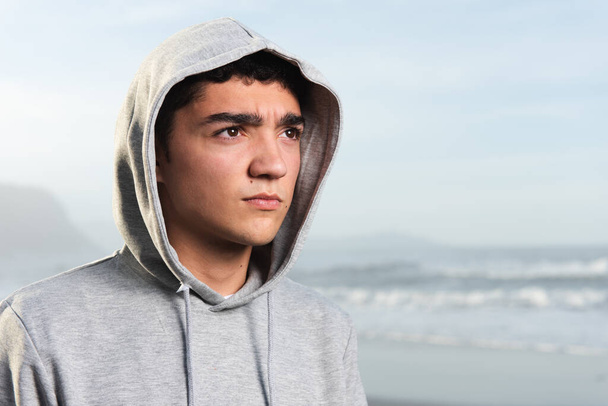 Portrait of serious handsome hispanic teenager wearing a hoodie at seaside - Photo, Image