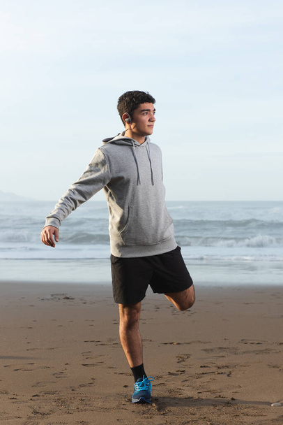 Hispanic teenager warming up before training at the beach - Foto, afbeelding