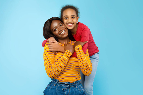 Αφρο-Αμερικανίδα που αγκαλιάζει τη χαμογελαστή μαμά της από πίσω - Φωτογραφία, εικόνα