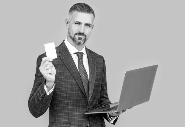 hombre de negocios seguro en traje de negocios celebrar portátil y tarjeta de débito, compras en línea - Foto, Imagen
