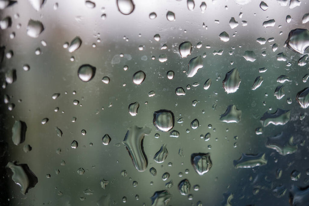 abstraktní pozadí zobrazující okno s kapkami deště valící se z modré tónované - Fotografie, Obrázek