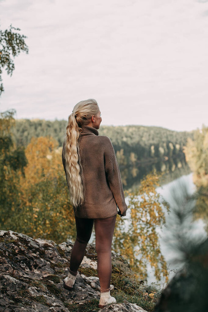 A young blonde girl walks in the autumn in the mountains with a view of the river and forest - Photo, Image