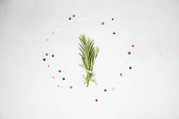 Un ramo de romero en un círculo de sal y granos de pimienta de colores. Estilo estacional. Comida natural y concepto cosmético. Fondo verde - Foto, Imagen