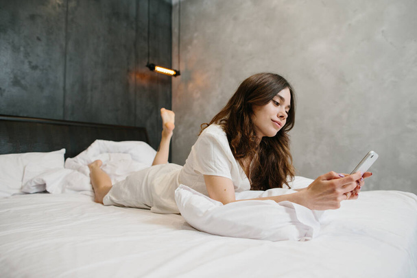 Розслаблена молода жінка використовує мобільний телефон в ліжку - стокове фото
 - Фото, зображення
