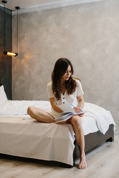 Όμορφη γυναίκα που γράφει σημειώσεις στο κρεβάτι στο σπίτι - φωτογραφία αρχείου - Φωτογραφία, εικόνα