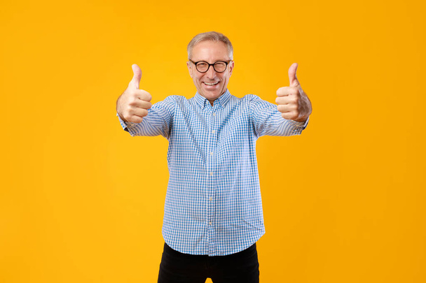 Happy mature guy gesturing thumbs up and smiling at studio - Фото, изображение