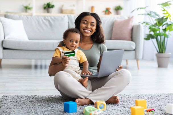 Online πληρωμές. Μαύρη μητέρα και βρέφος μωρό χρησιμοποιώντας φορητό υπολογιστή και πιστωτική κάρτα - Φωτογραφία, εικόνα