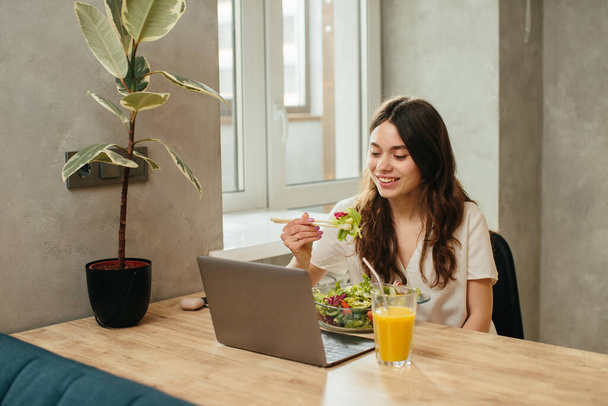 Young woman eating salad while sitting in kitchen - stock photo - Photo, Image