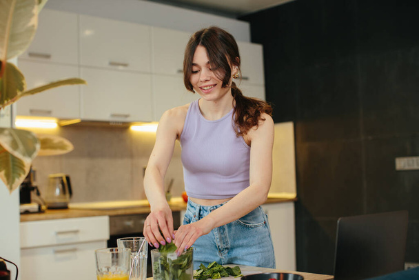 Jovem mulher preparando smoothie verde saudável na cozinha - Foto, Imagem
