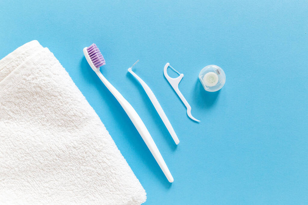 Flatlay of white towel, toothbrush, dental floss and other toiletries on a blue background. Morning routine and oral mouth and teeth hygiene concept - Foto, Bild