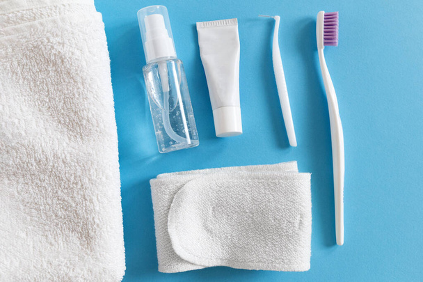 Flatlay of toothbrush and paste, cosmetics and towel on a blue background. Morning routine for women everyday hygiene concept - Фото, зображення