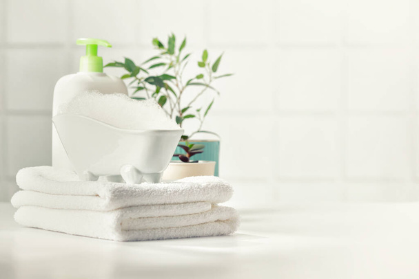 A miniature bubble bath, shampoo, flowers and white towels on bathroom countertop - Fotografie, Obrázek