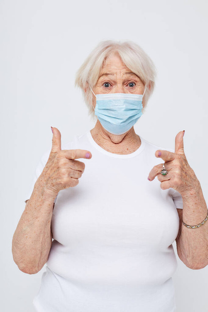 Portrait of an old friendly woman health lifestyle medical mask treatment light background - 写真・画像