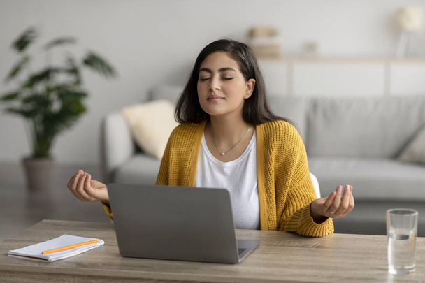 Workplace stress management. Calm arab woman meditating with closed eyes in front of laptop, sitting at desk - Zdjęcie, obraz