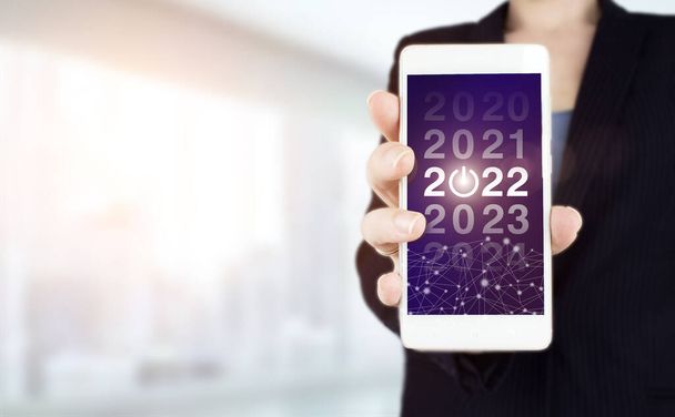 Koncepció Új Év 2022. Kézi fehér okostelefon digitális hologram 2022 jel a fény homályos háttér. A látás koncepciója 2021-2022. Üzletember üdvözlő év 2022 - Fotó, kép