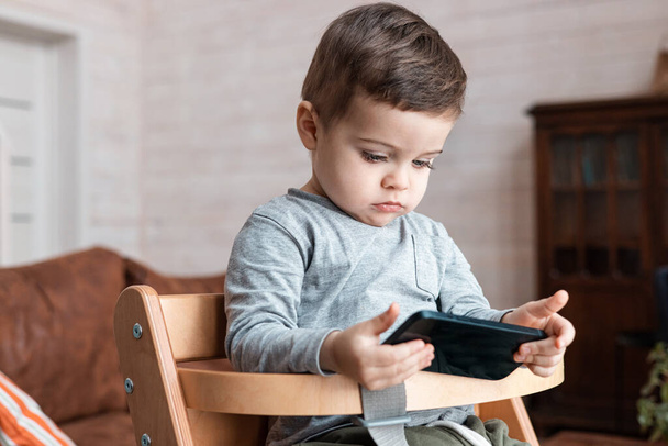 Cute little toddler boy playing with smartphone Healthy baby touching mobile phone with fingers, looking cartoons and having fun with educational apps. Child at home - Foto, Imagem