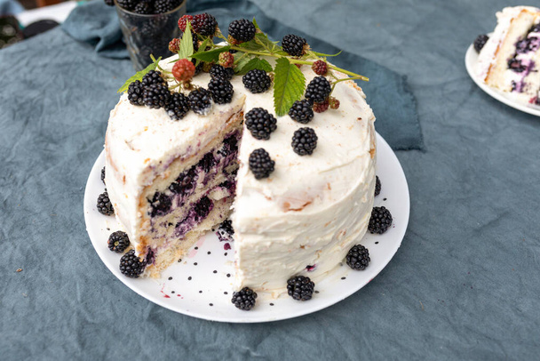 Delicious rustic cake with buttercream frosting and decorated with blackberry. One piece is cut off - Zdjęcie, obraz