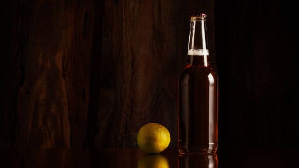 Full bottles of beer and lime, against a dark wooden wall - 写真・画像