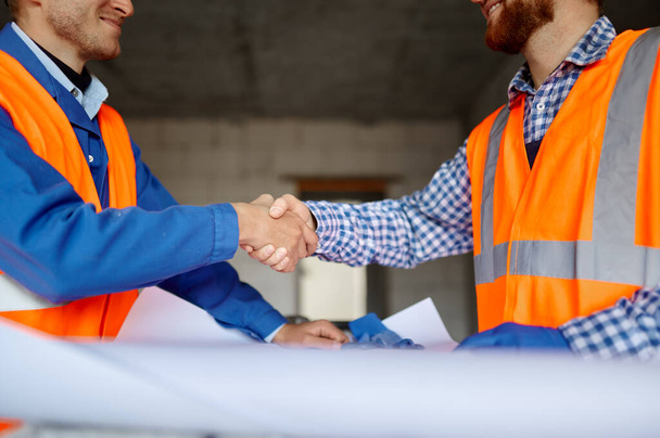 Builder and engineer handshake over paper blueprint - 写真・画像