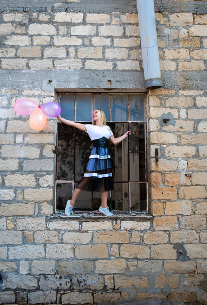 Mujer feliz divirtiéndose sosteniendo globos de aire de colores en una ventana rota - Foto, Imagen