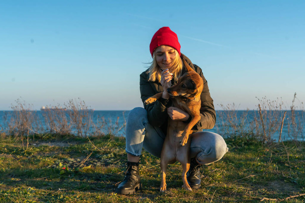 A blonde girl with a purebred dog from the shelter. Playing with a dog on the seashore. Friendship of a dog and a person - Foto, afbeelding
