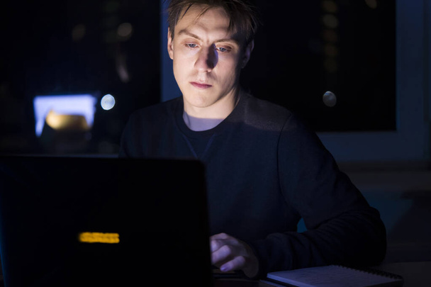 Ο άνθρωπος εργάζεται σε ένα φορητό υπολογιστή τη νύχτα. - Φωτογραφία, εικόνα
