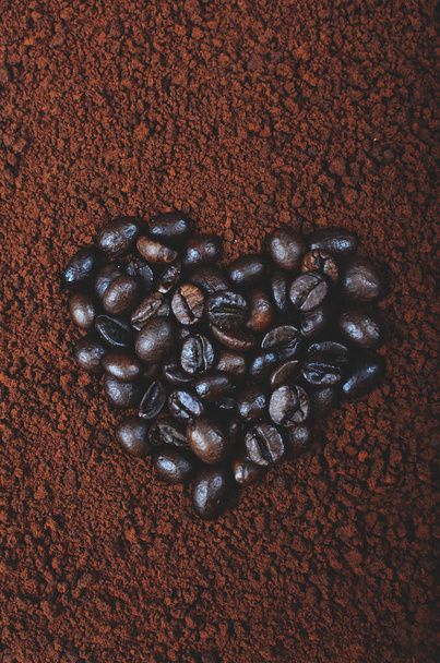 Heart shaped coffee beans over artificial instant coffee powder. - Zdjęcie, obraz